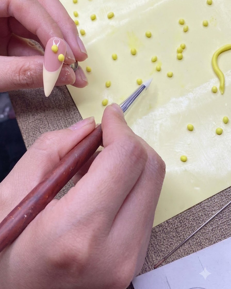 Un pinceau en silicone transférant une petite boule de gel jaune sur une capsule dentraînement de couleur nude.