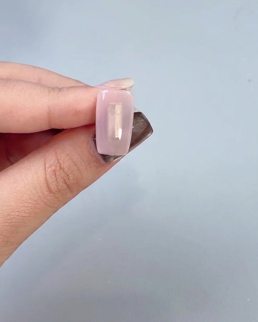 Gros plan dune main appliquant un gel de base transparent sur la surface dun ongle avec un pinceau.