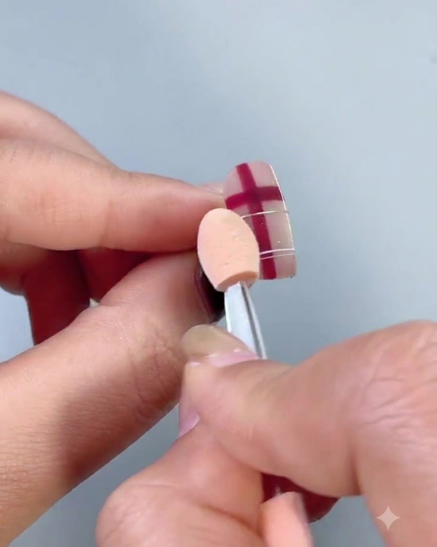 Un pinceau à poussière blanc et duveteux balayant les particules de poudre métallique en suspension sur un ongle décoré.