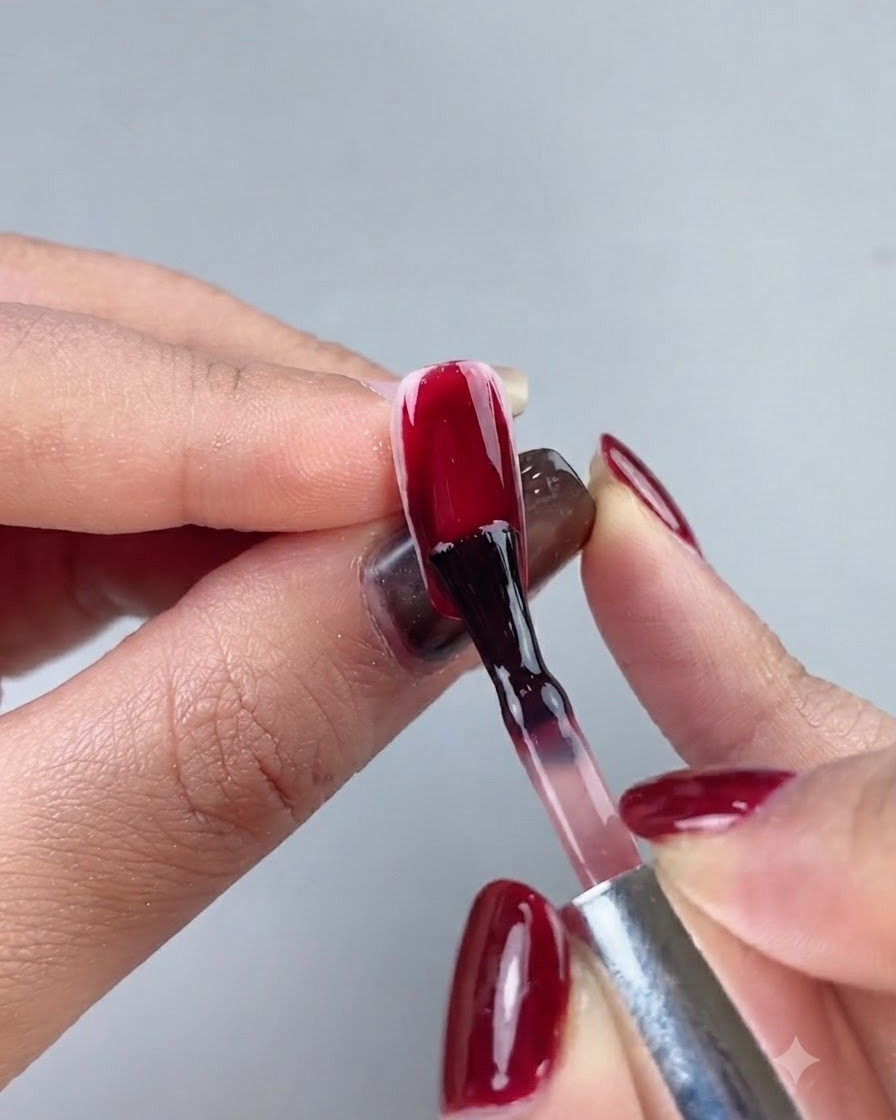 Un pinceau à ongle appliquant un vernis gel rouge oxblood profond sur une extension dongle complète.