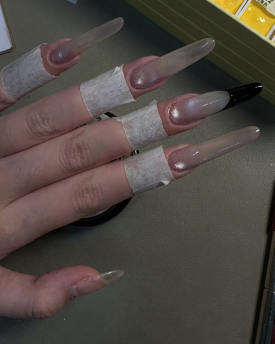 Une main présentant quatre longs ongles stiletto parachevés dun look scintillant œil-de-chat gris nacré.