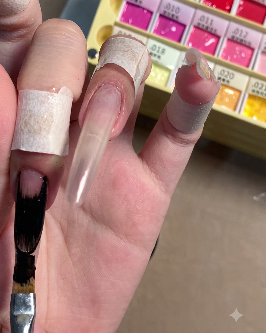 Un pinceau plat pour nail art appliquant un vernis gel noir opaque sur lextrémité allongée dun ongle stiletto transparent.