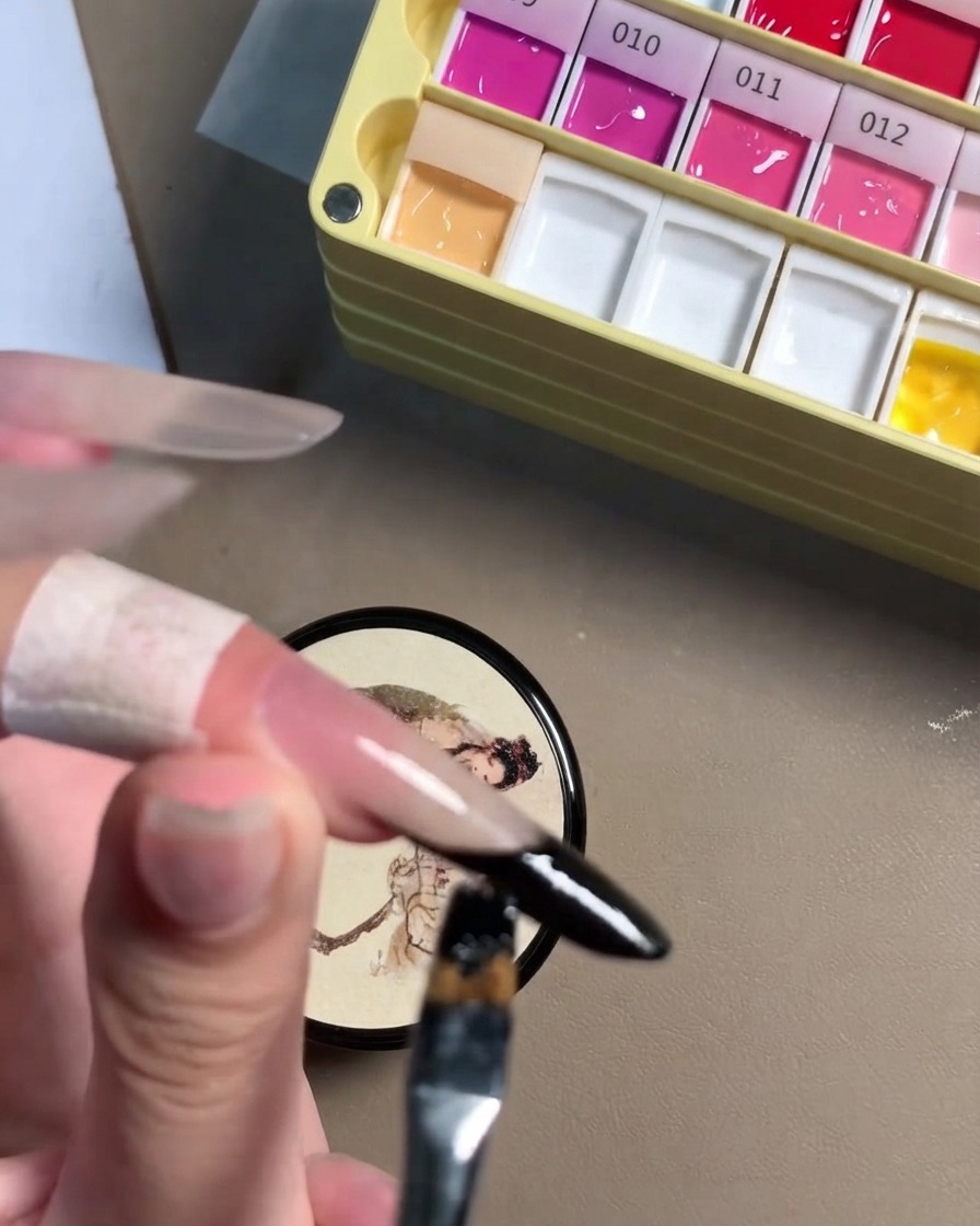 Une vue rapprochée dun pinceau de détail parachevant la ligne en gel noir sur le rebord dun ongle stiletto.