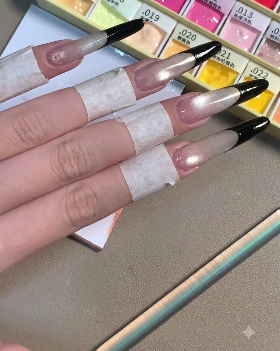 Quatre longs ongles stiletto arborant des French tips noires profondes achevées sur une base grise chatoyante.