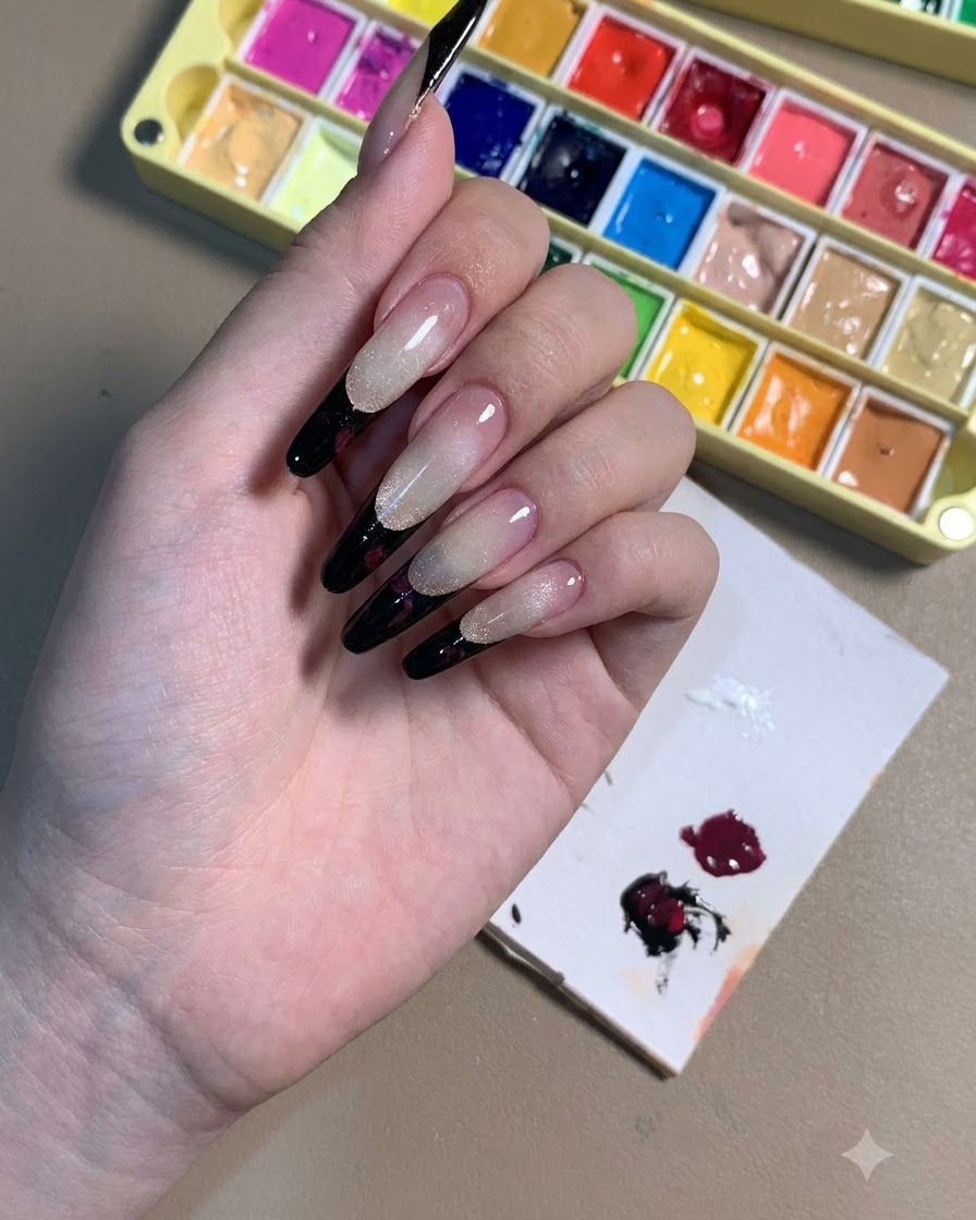 Une main présentant des ongles stiletto ornés de French tips noires et de contours de roses prune foncé.