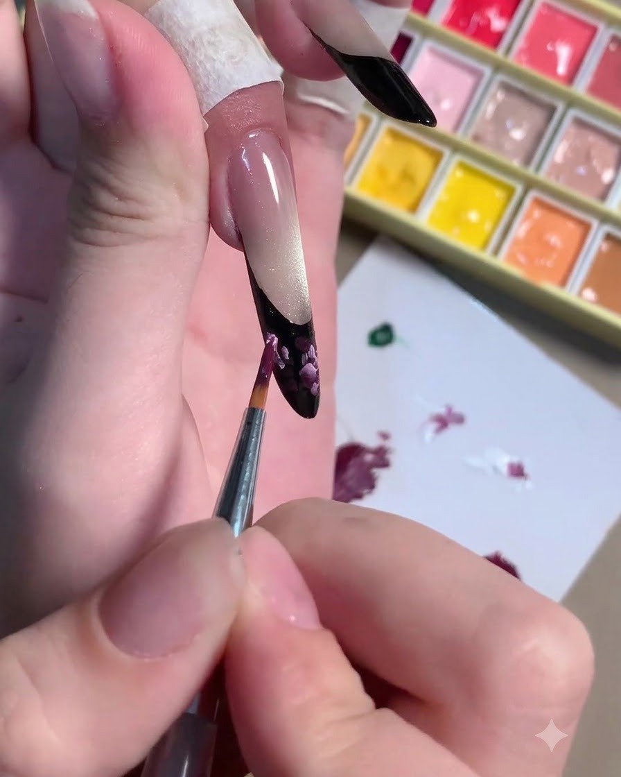 Un pinceau fin appliquant des traits de lumière rose clair par-dessus le nail art floral prune foncé.