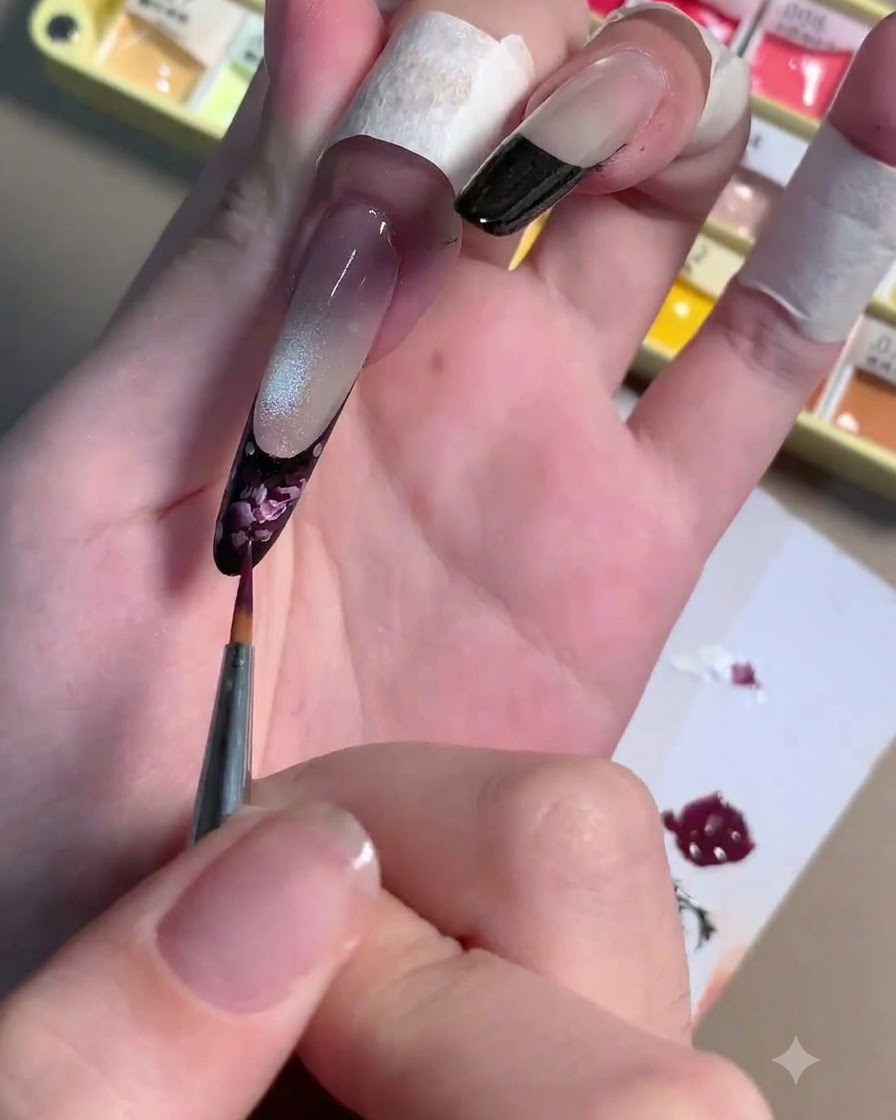 Un pinceau liner fin appliquant des traits de gel rose clair par-dessus une base de rose prune foncé sur un ongle.