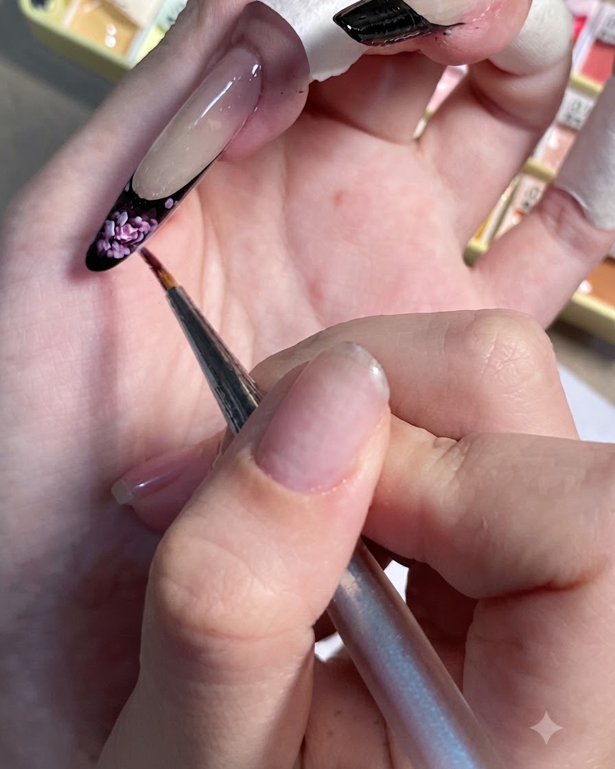 Un pinceau de précision parsemant de minuscules touches rose clair sur la French tip noire dun ongle peint.