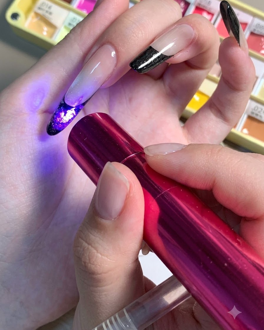 Une mini lampe UV/LED rouge maintenue au-dessus dun ongle pour catalyser les détails du cœur sombre dun design floral.