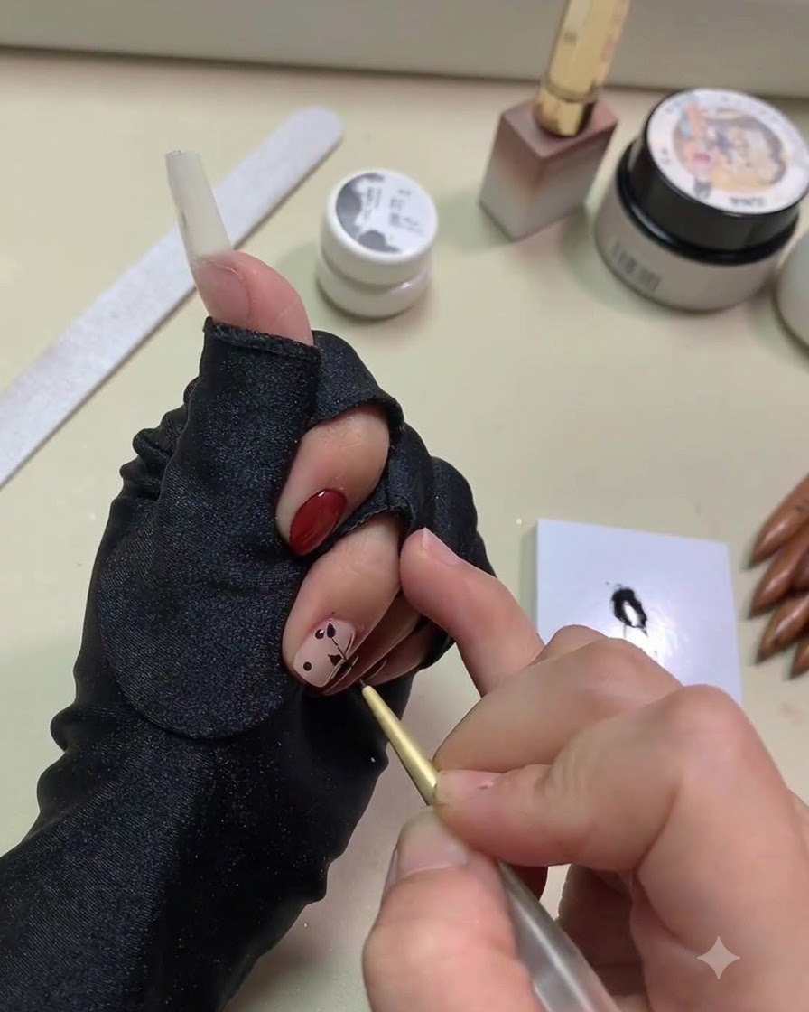 Gros plan dune main utilisant un pinceau liner doré fin pour étirer du gel noir en formes de feuilles à partir de points sur un ongle à base nude.
