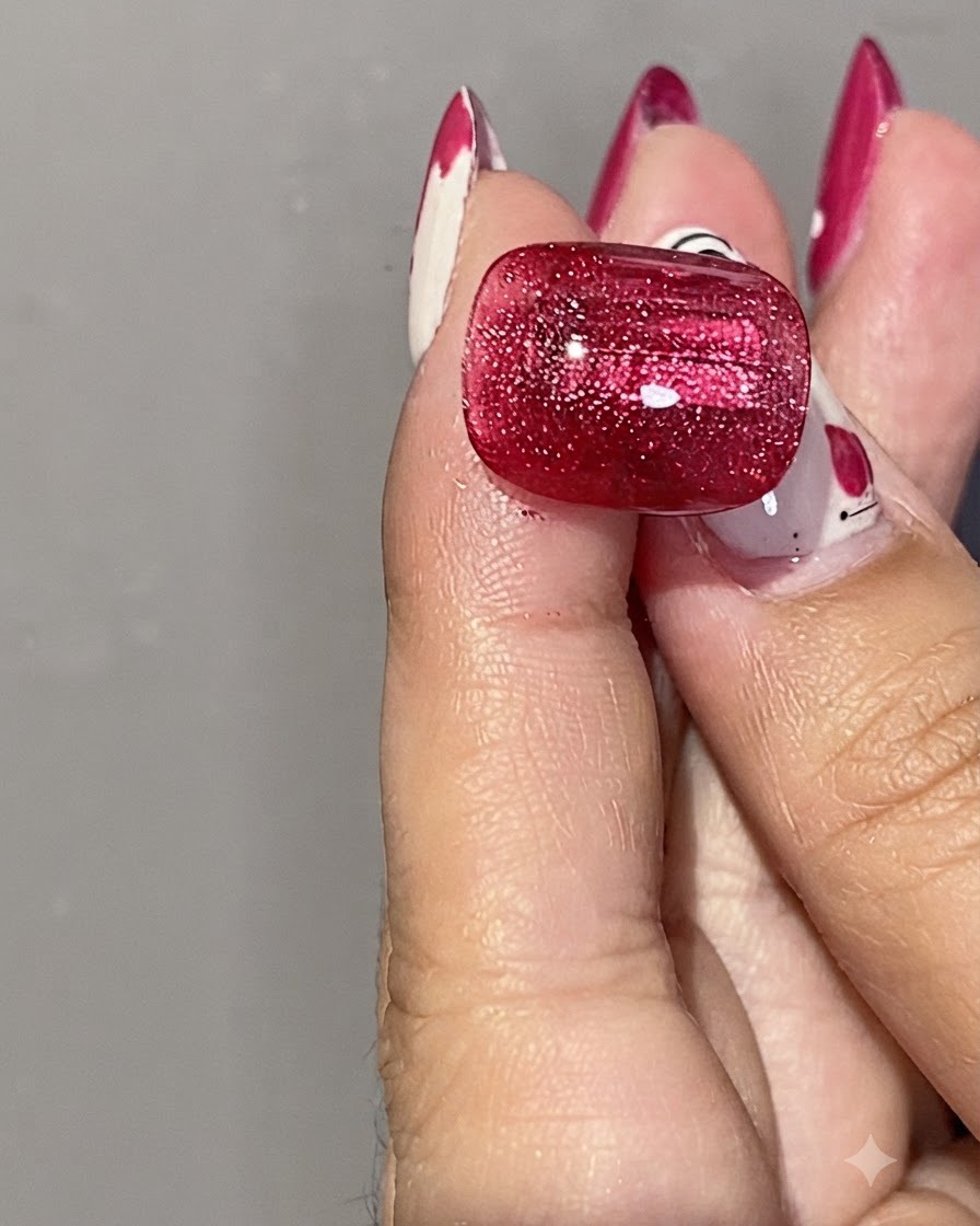 Gros plan dune main tenant un aimant cylindrique argenté près dun ongle en gel cat eye rouge brillant pour modeler le reflet.