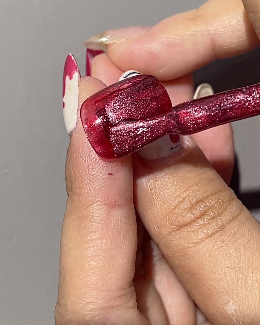 Un pinceau appliquant une seconde couche de gel cat eye rouge scintillant sur un ongle déjà peint en rouge.