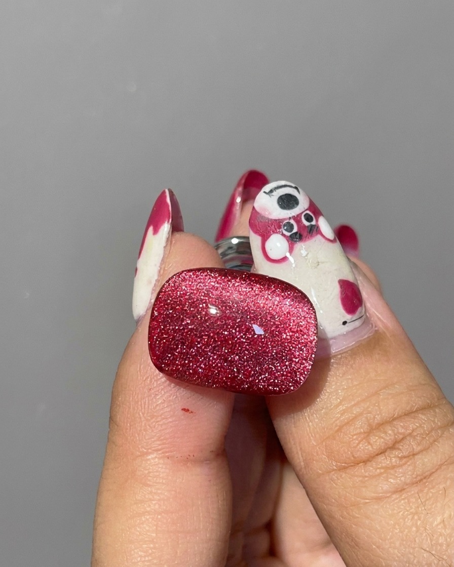 Gros plan dun aimant cylindrique argenté tenu près des bords dun ongle couvert de gel cat eye rouge humide pour déplacer les paillettes.