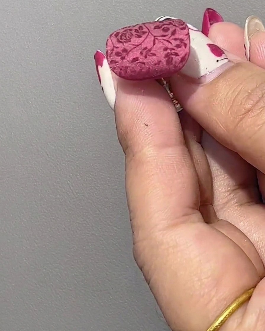 Gros plan dun ongle manucuré affichant un motif floral rouge transféré sur une base brillante non catalysée.