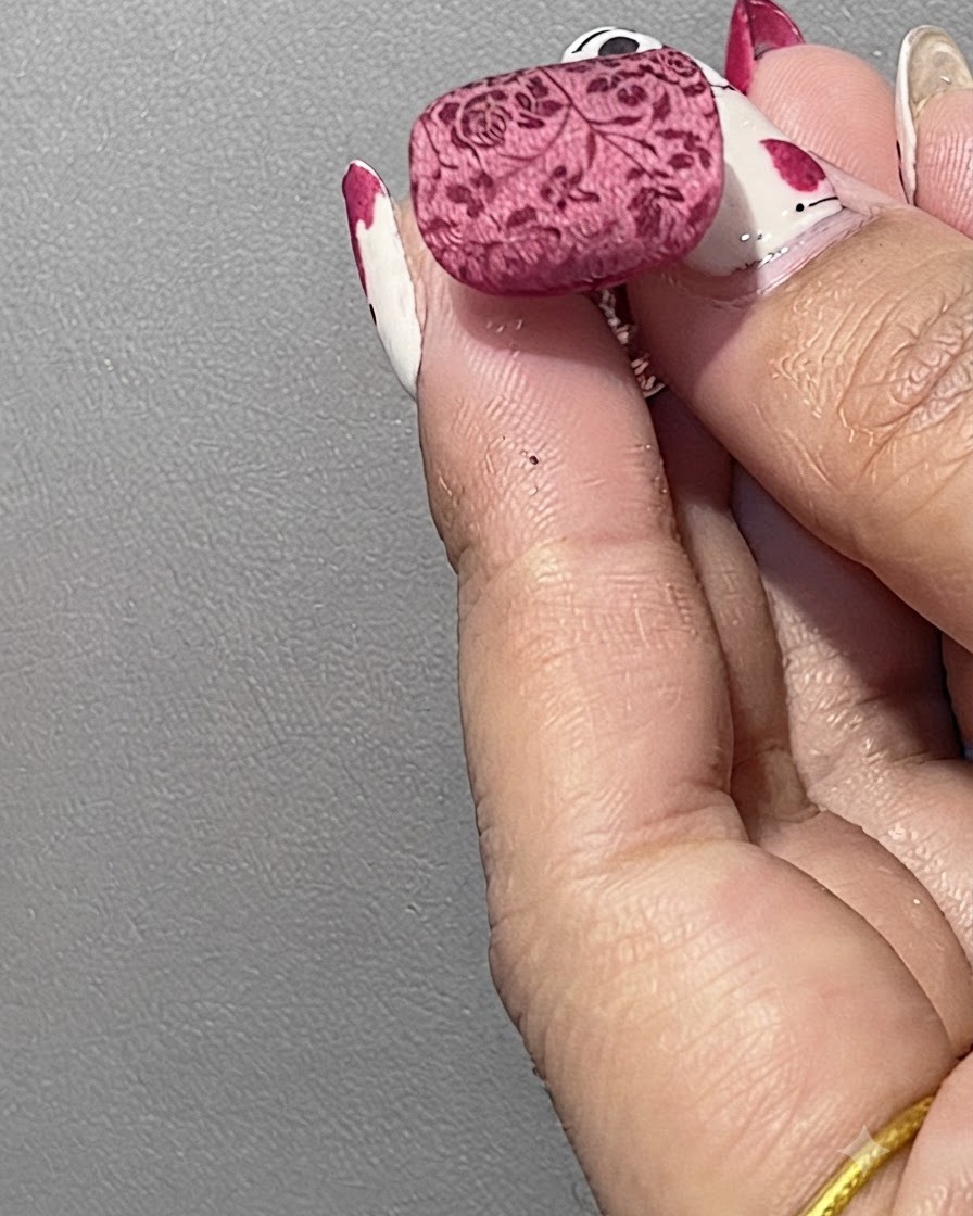 Un ongle manucuré positionné sous une lumière de polymérisation pour fixer le motif floral recouvert de poudre.