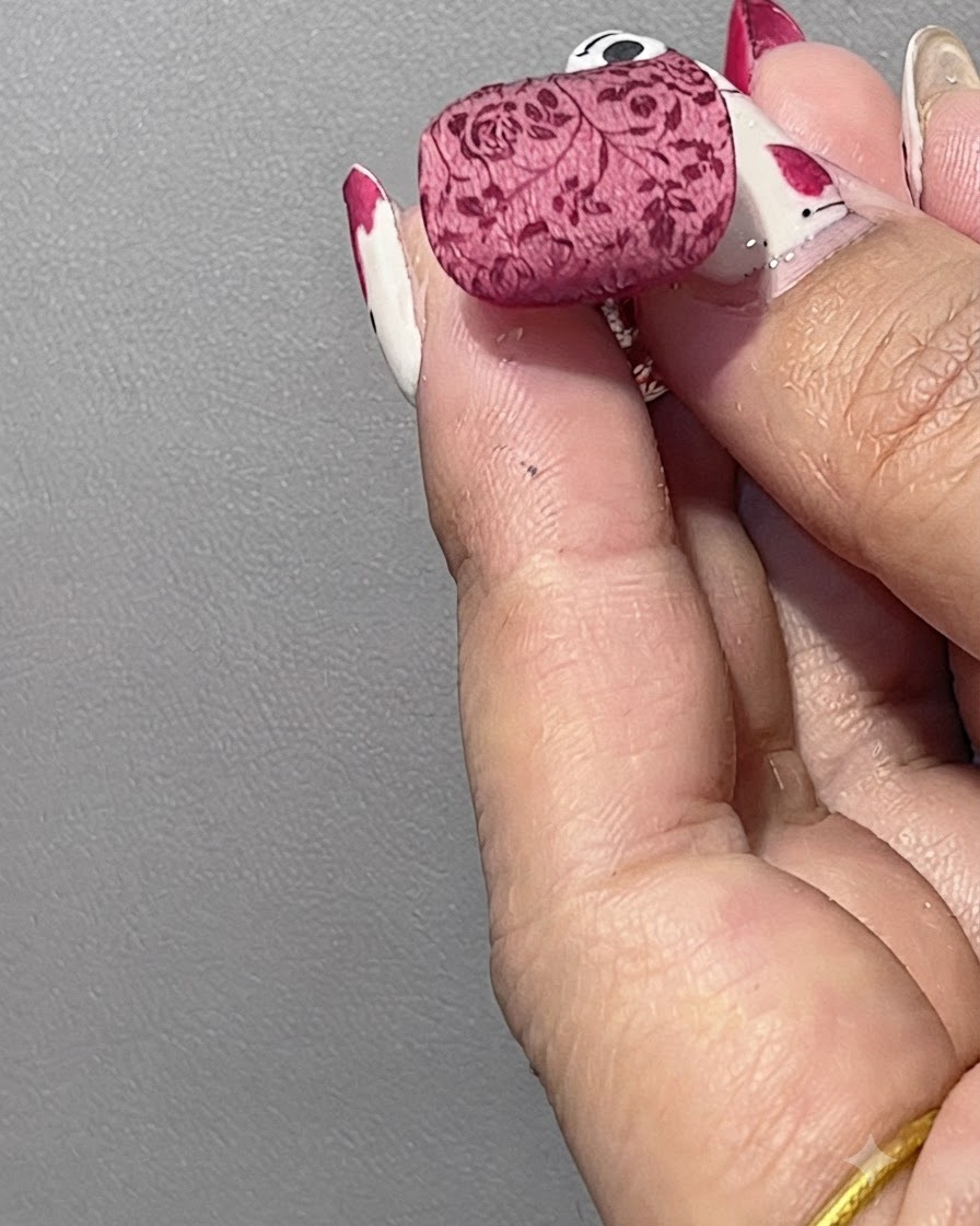 Un pinceau touffu balayant la poudre blanche libre dun ongle terminé montrant un doux motif floral poudré.