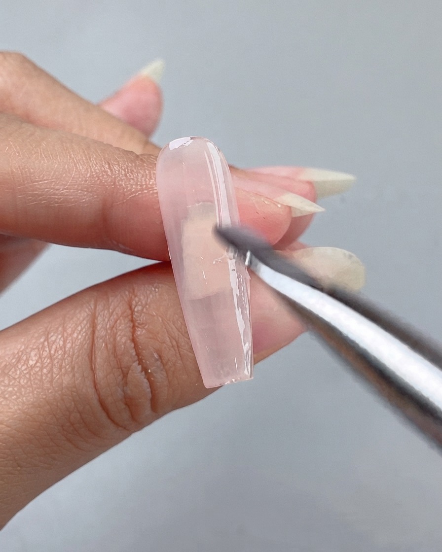 Gros plan dun pinceau plat appliquant une base de gel rose transparent Jade 1 sur un long ongle nu.