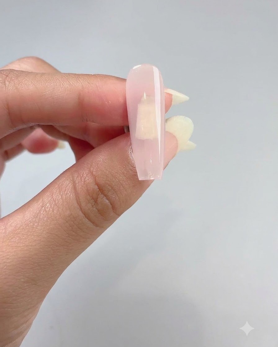 Gros plan dune main tenant une capsule dongle recouverte dun gel de base rose doux et translucide.