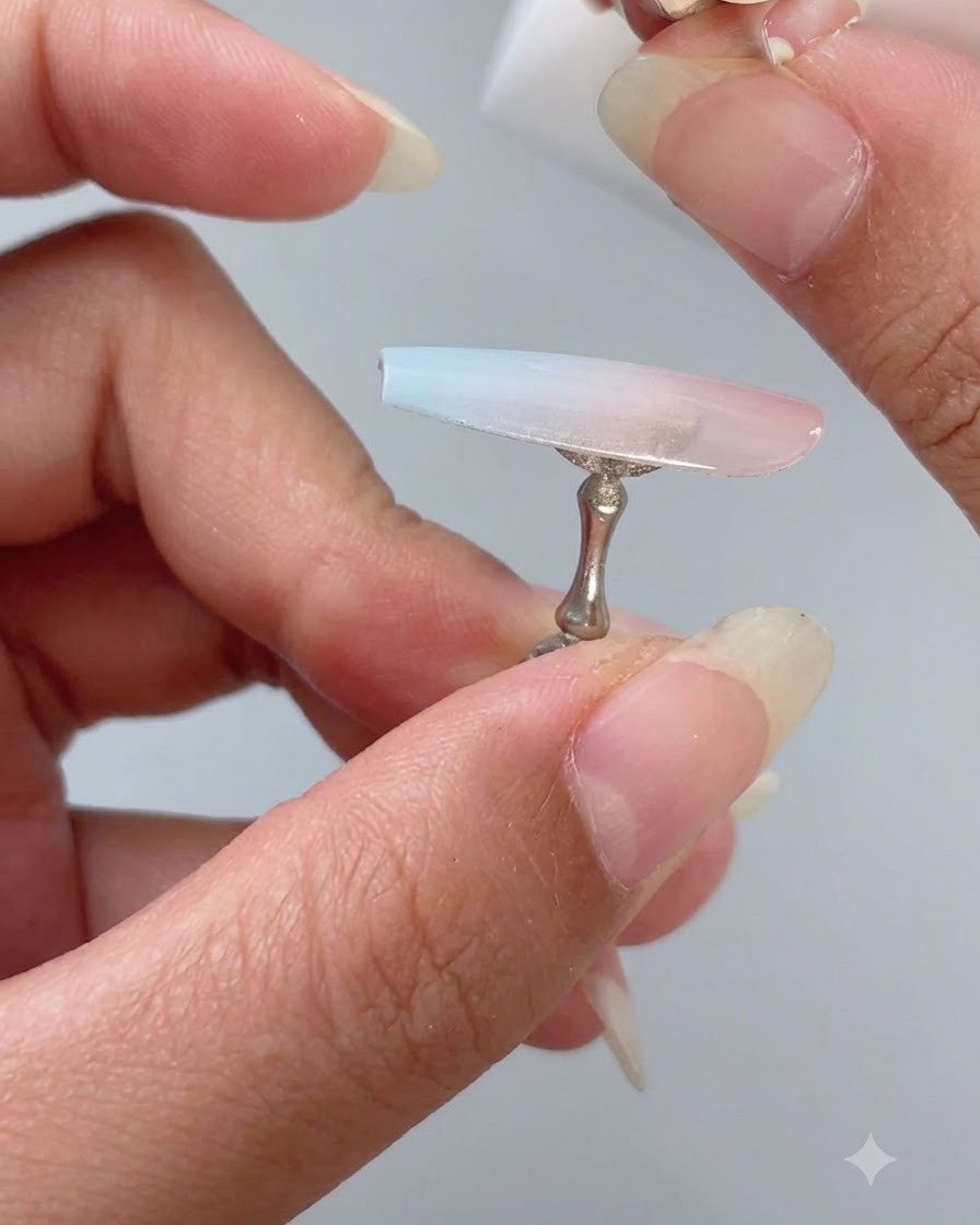 Une main utilisant un petit morceau déponge blanche pour tapoter du vernis gel bleu clair sur la moitié inférieure dune capsule dongle.