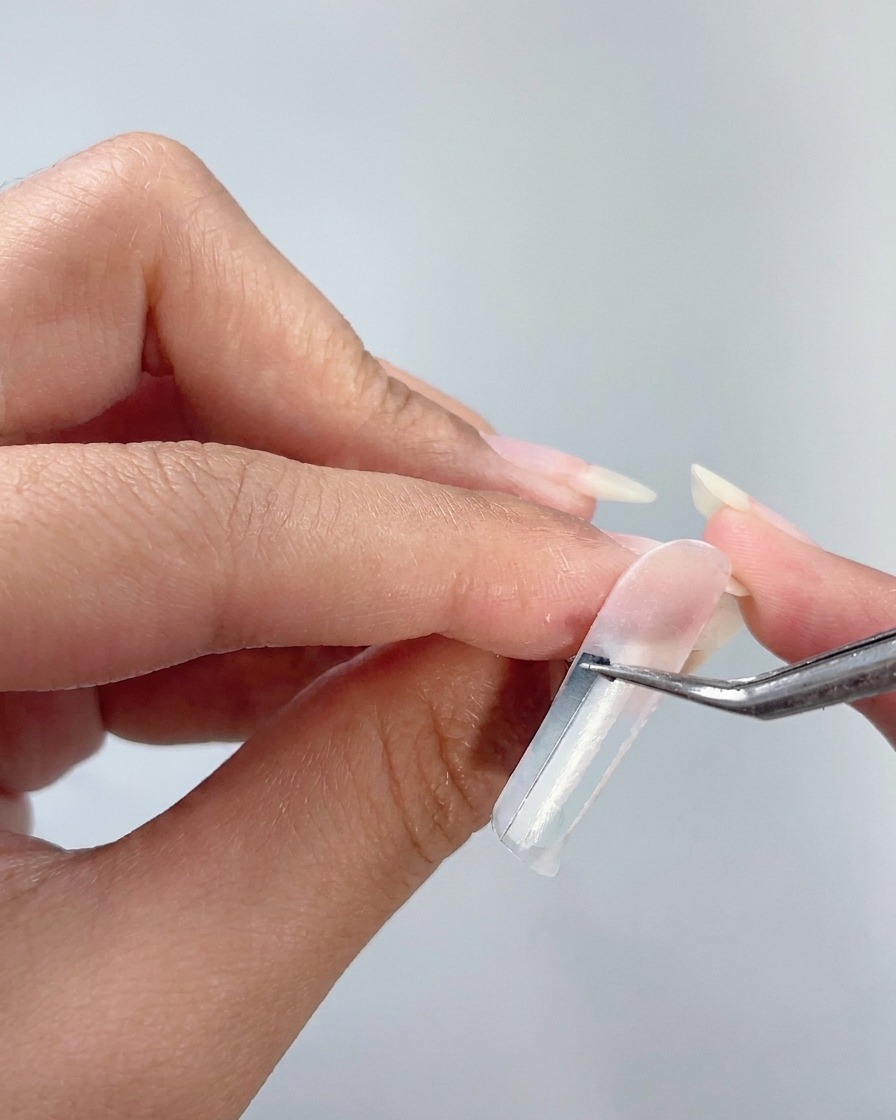 Une pince à épiler retirant une bande verticale dun ongle pour révéler des rayures blanches nettes.