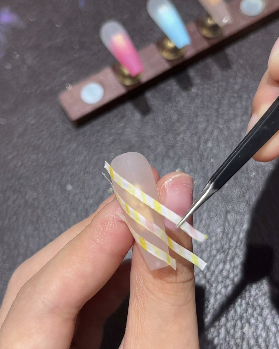 Un gros plan de brucelles appuyant le ruban de striping à plat sur un ongle.