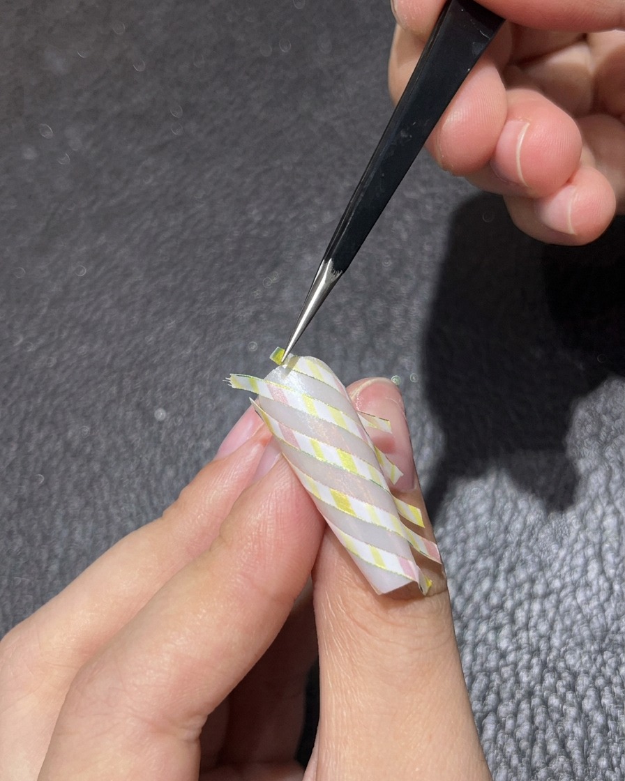 Des brucelles retirant délicatement le ruban de striping diagonal dun ongle à motif.
