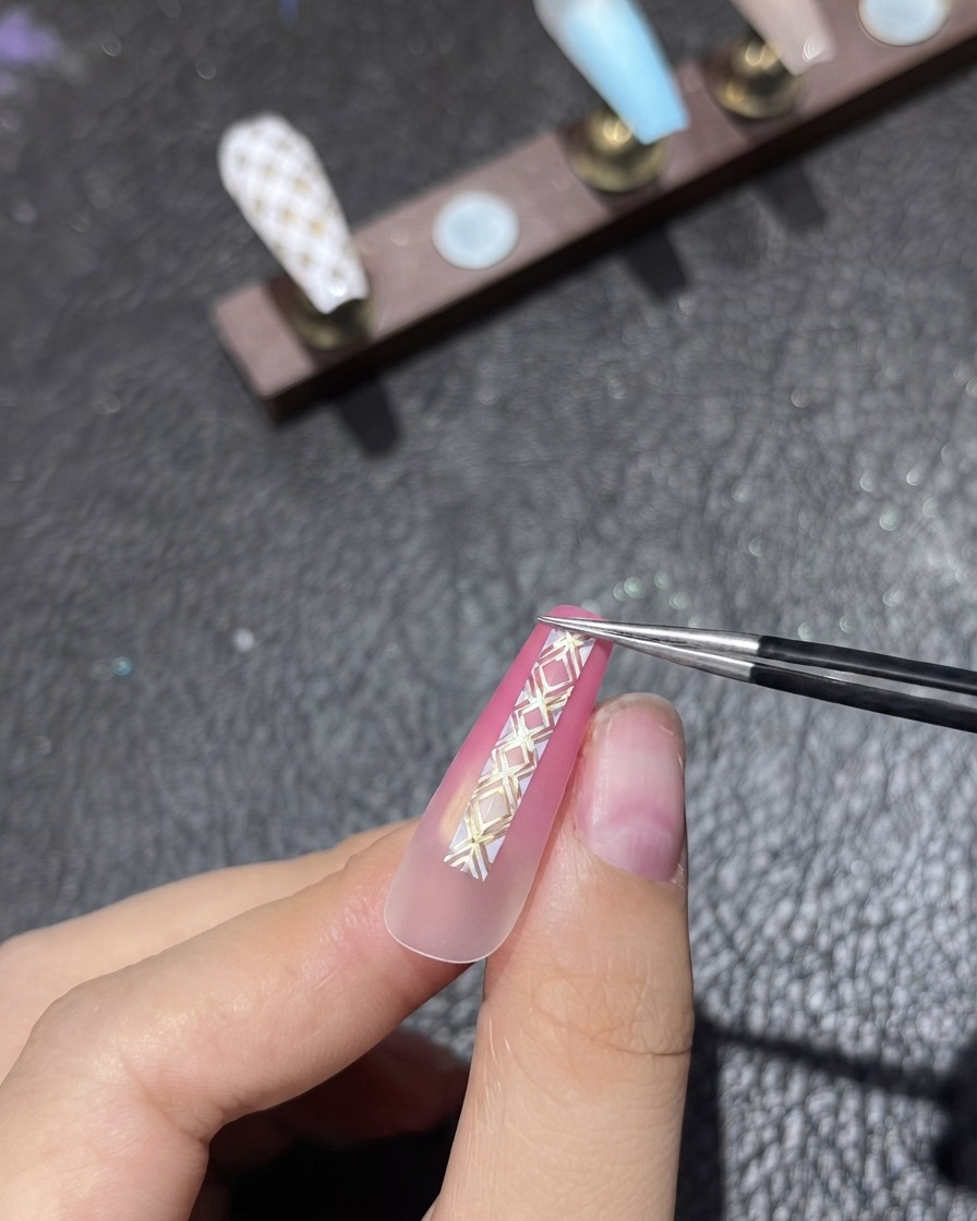 Une paire de brucelles plaçant soigneusement du ruban de striping vertical sur un ongle rose dégradé.
