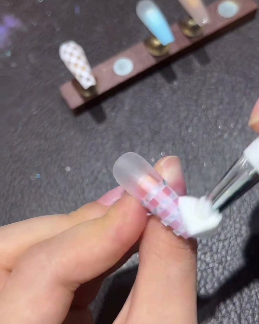 Un outil éponge appliquant du vernis gel blanc en le tamponnant sur des bandes de ruban horizontal sur un ongle dégradé rose.