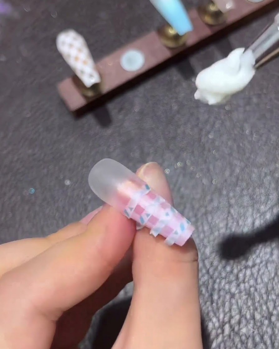 Un petit pinceau de nail art survolant avec une couche de finition transparente un ongle écossais dégradé rose et bleu terminé.