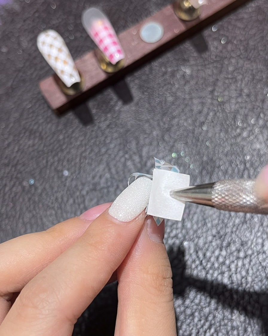 Un outil éponge appliquant du gel dab blanc sur le ruban de striping diagonal dun ongle manucuré.