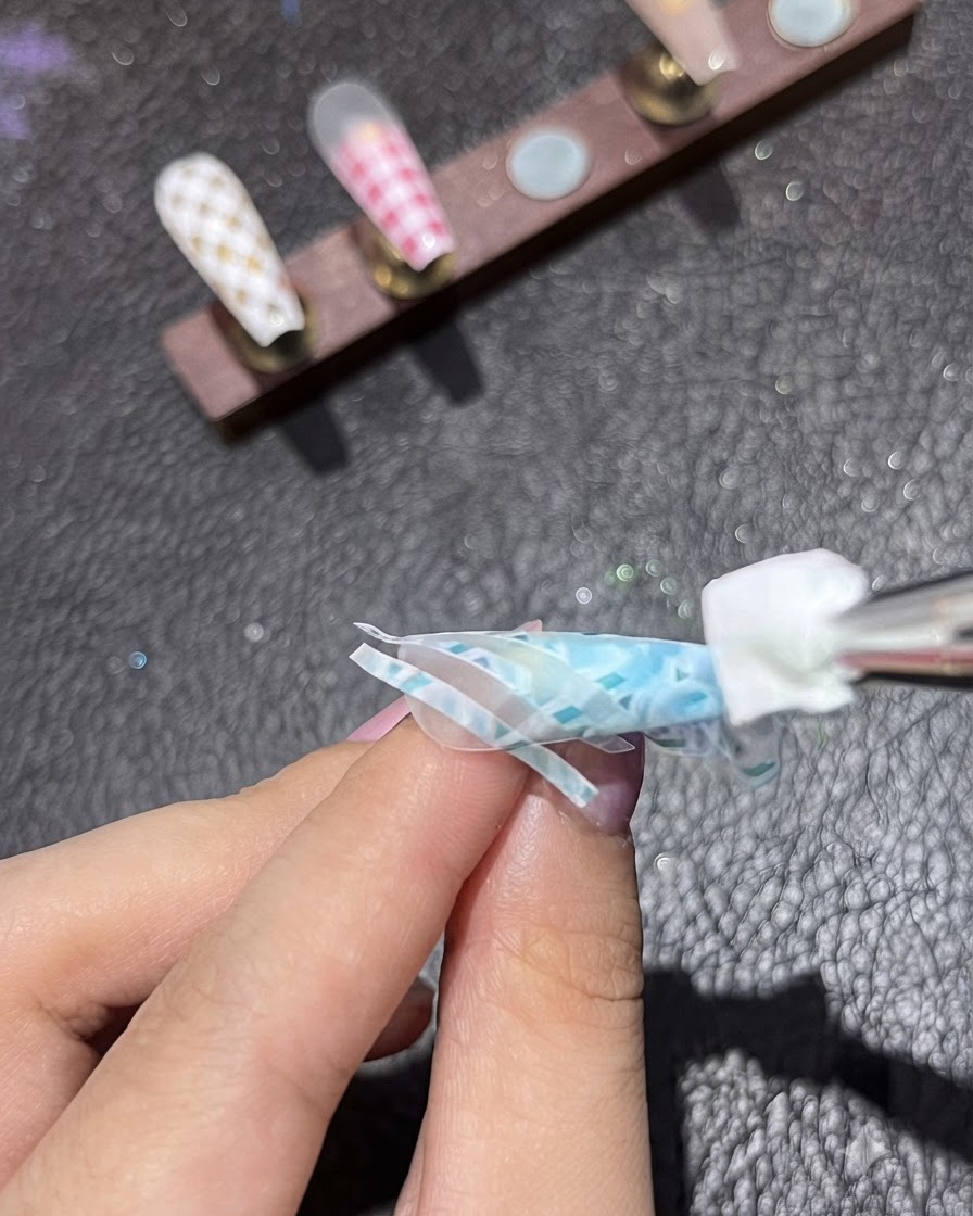 Un outil éponge appliquant du pigment blanc sur une deuxième couche de ruban de striping sur un design dongle bleu.