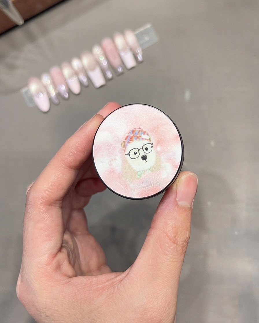 Un pinceau à gel appliquant du vernis gel cat-eye argenté étincelant sur la moitié supérieure dun ongle.