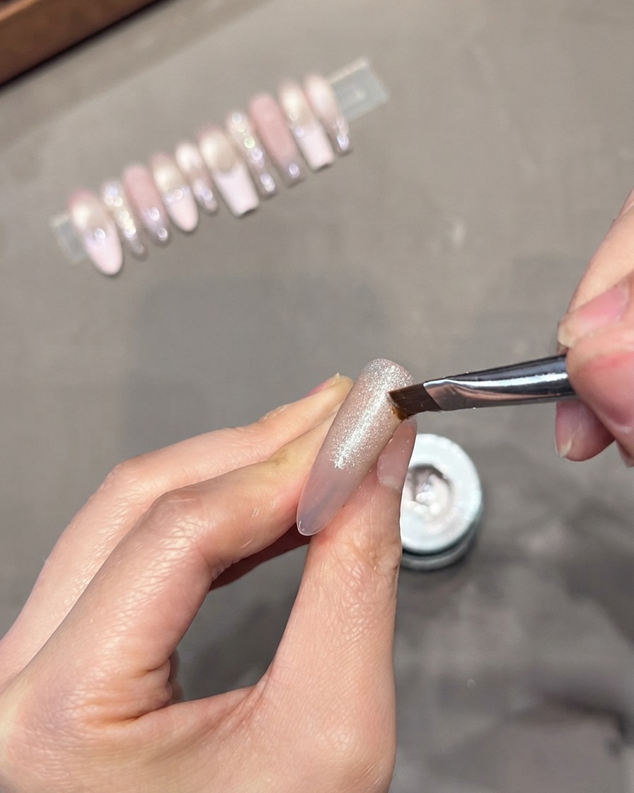 Un pinceau plat biseauté étirant et estompant le gel cat-eye argenté humide vers le bas sur une capsule dongle transparente.