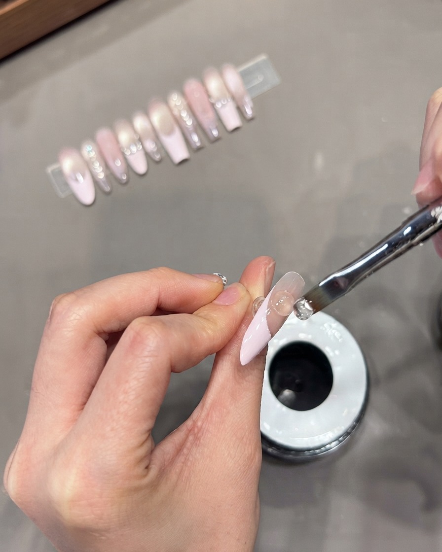 Utilisation dun pinceau à gel plat pour appliquer une perle de gel de construction transparent sur un design de French tip cat-eye.