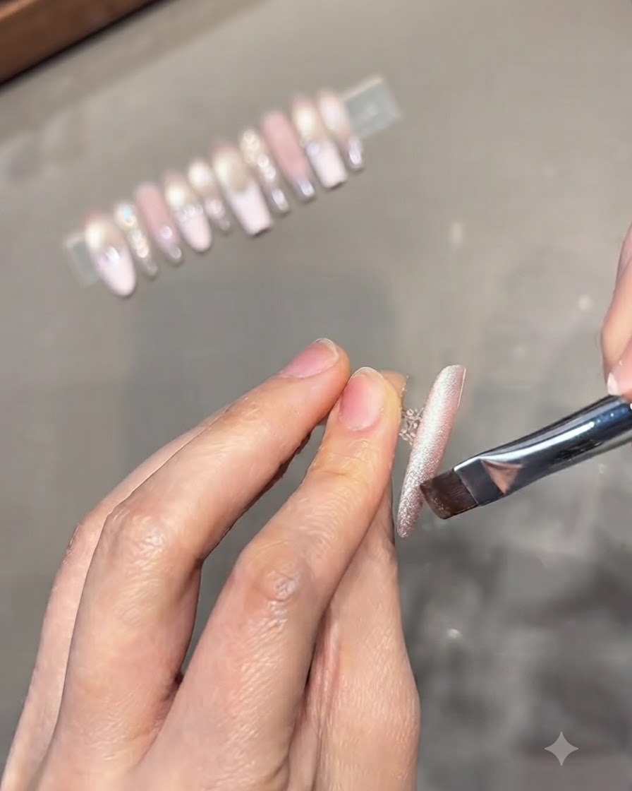 Un pinceau à ongle appliquant du vernis gel cat-eye argenté sur toute la longueur dun ongle dentraînement aux tons neutres.