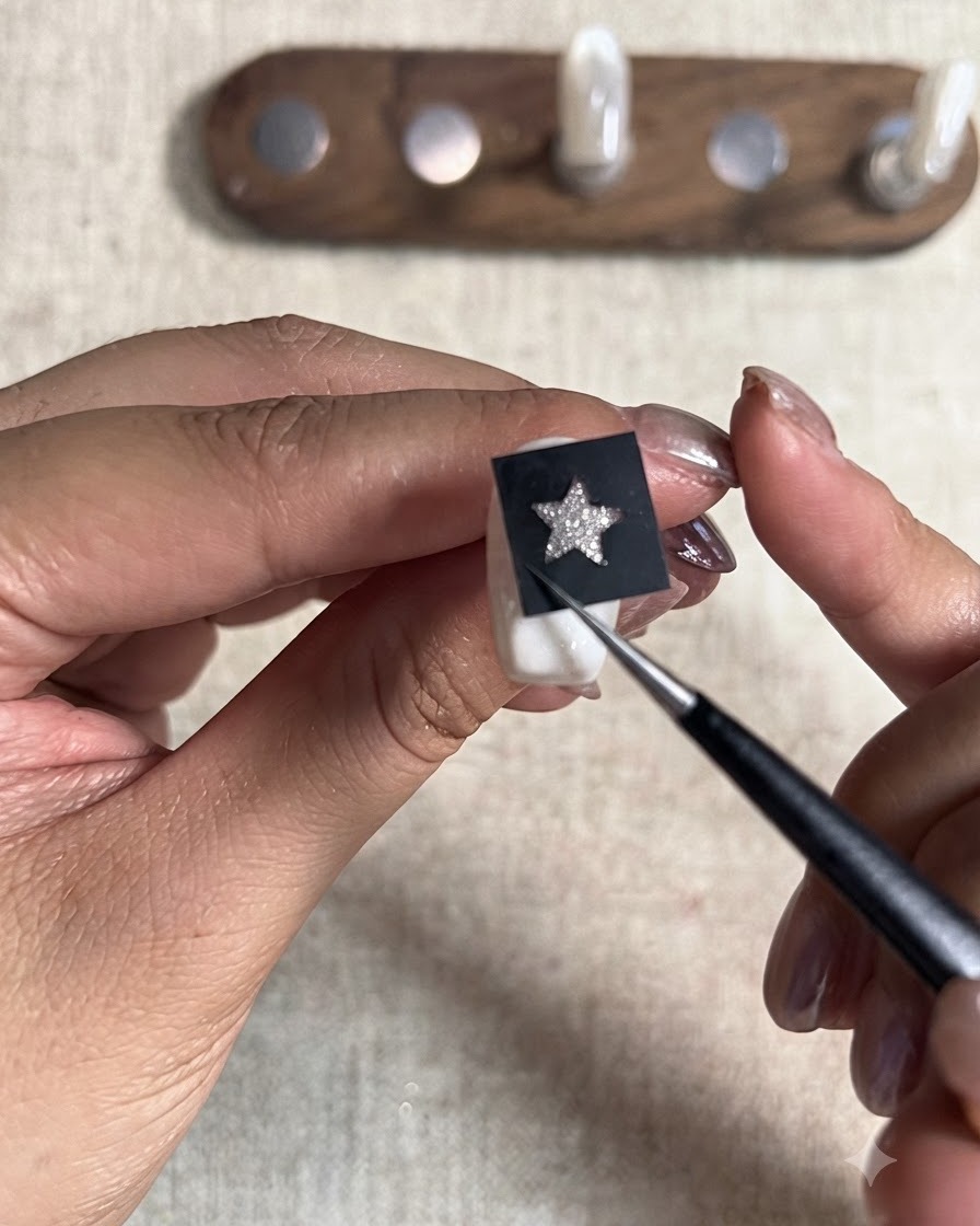 Un outil pointu pressant fermement un autocollant pochoir étoile noir placé sur la surface dun ongle peint.