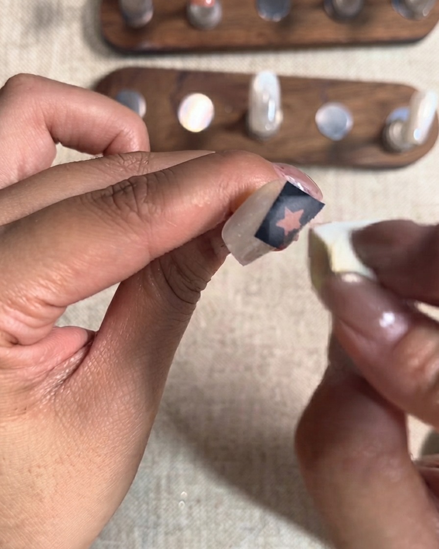 Une petite éponge cosmétique tamponnant une seconde couche de gel rouge sur un autocollant de découpe détoile sur un ongle.
