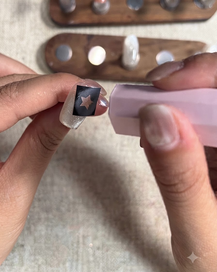 Une mini lampe de catalysation UV/LED rose maintenue au-dessus dun ongle avec un pochoir étoile pour durcir la couche finale de gel rouge.