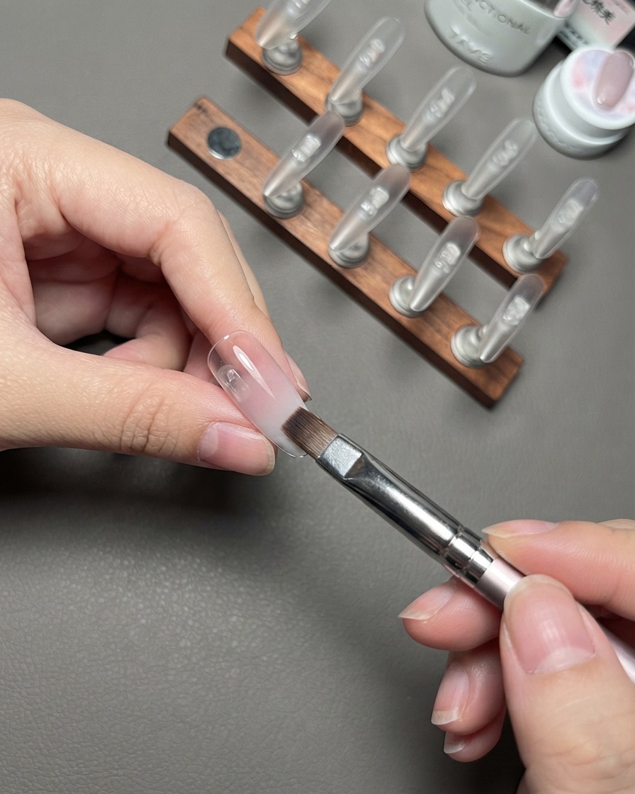 Un pinceau estompant la couche de dégradé nude sur un faux ongle.