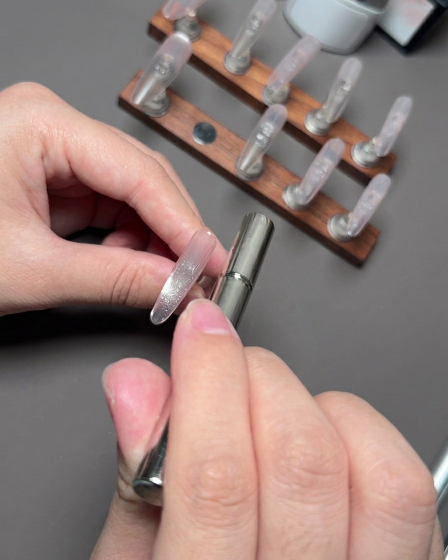 Un bâtonnet aimanté planant près dun ongle pour rassembler et façonner les particules réfléchissantes cat eye.
