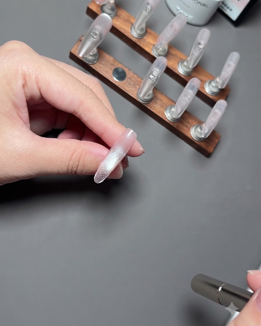 Une main tenant un ongle devant un fond sombre pendant que le gel cat eye catalyse sous la lumière.