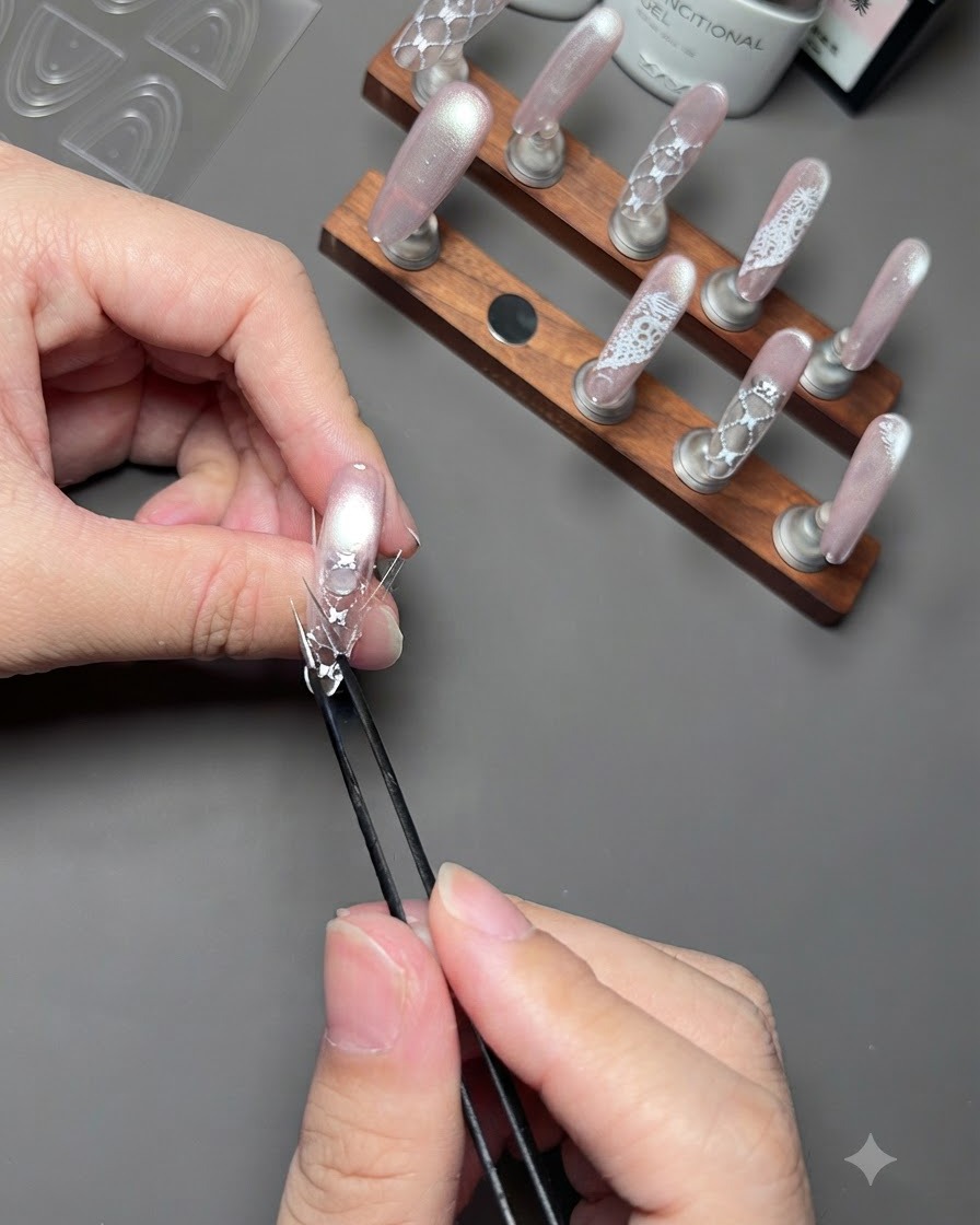 Une paire de brucelles pressant les bords dun autocollant incurvé sur un ongle décoré fixé sur un présentoir.