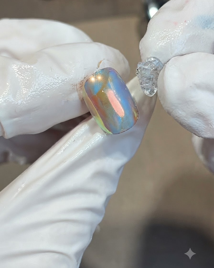 Dépôt dune noisette de gel bonbon doux, épais et transparent, au centre dun ongle irisé orange et bleu.