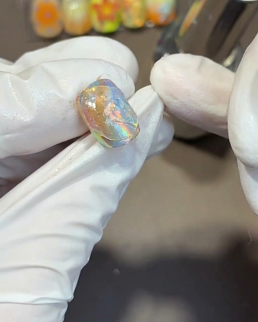 Utilisation dun outil métallique pour creuser des textures fluides et ondulées dans le gel transparent épais sur un ongle irisé.