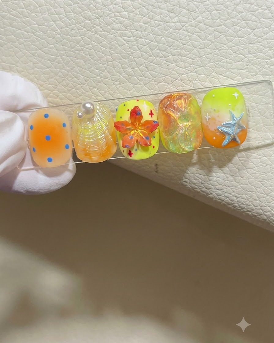 Une main gantée tenant un présentoir à ongles présentant cinq designs dongles colorés sur le thème de lété.