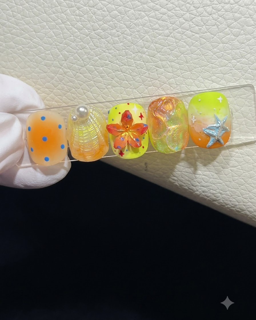 Gros plan sur un présentoir à ongles mettant en valeur cinq press-on nails sur le thème de lété dotés de diverses textures 3D et décorations.