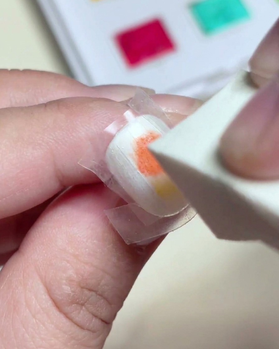 Une éponge à maquillage tapotant doucement sur le gel rouge et jaune humide pour créer un dégradé homogène.