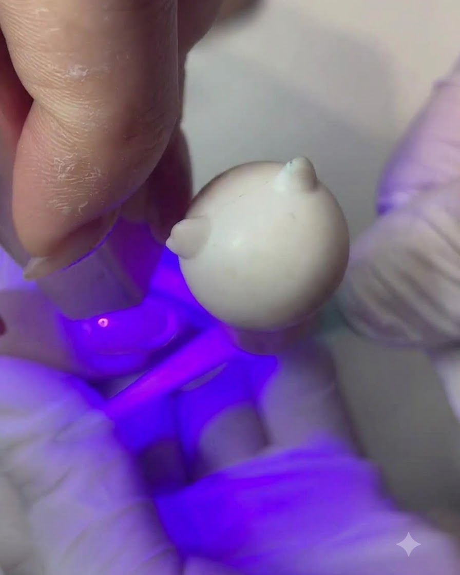 Un pinceau fin appliquant une fine couche de gel couleur pêche nude sur un ongle.