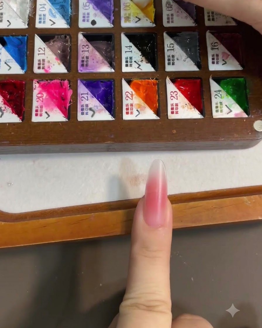 Gros plan dun pinceau prélevant du gel jaune vif sur une palette de peintre compartimentée, avec un ongle blush rose en premier plan.