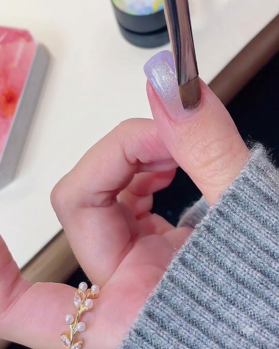 Un pinceau à ongles ou un outil magnétique planant au-dessus dun ongle en gel violet et scintillant effet œil de chat.